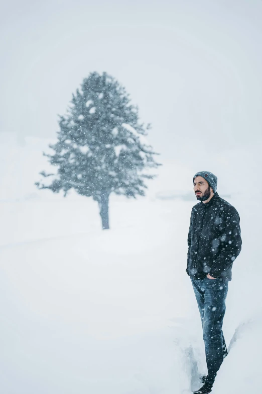 a man standing in the snow next to a tree