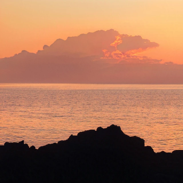 a lone boat in the ocean on a rocky shore at sunset