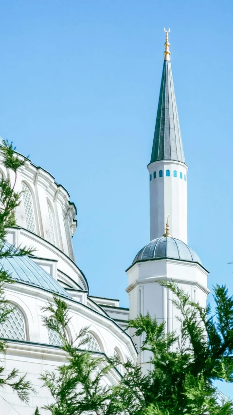 the top of a building with a spire next to green foliage