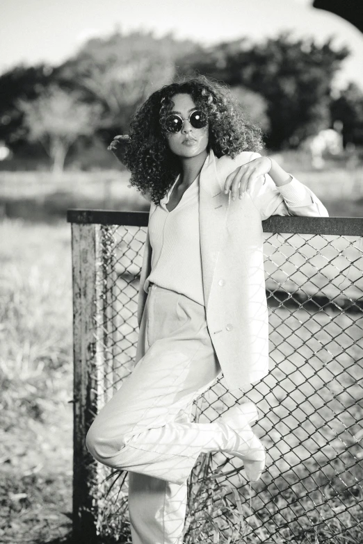 a woman posing in front of a fence wearing sunglasses