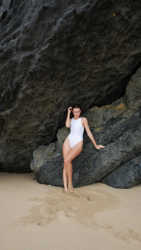 a woman in a white bathing suit standing on the sand next to large rocks