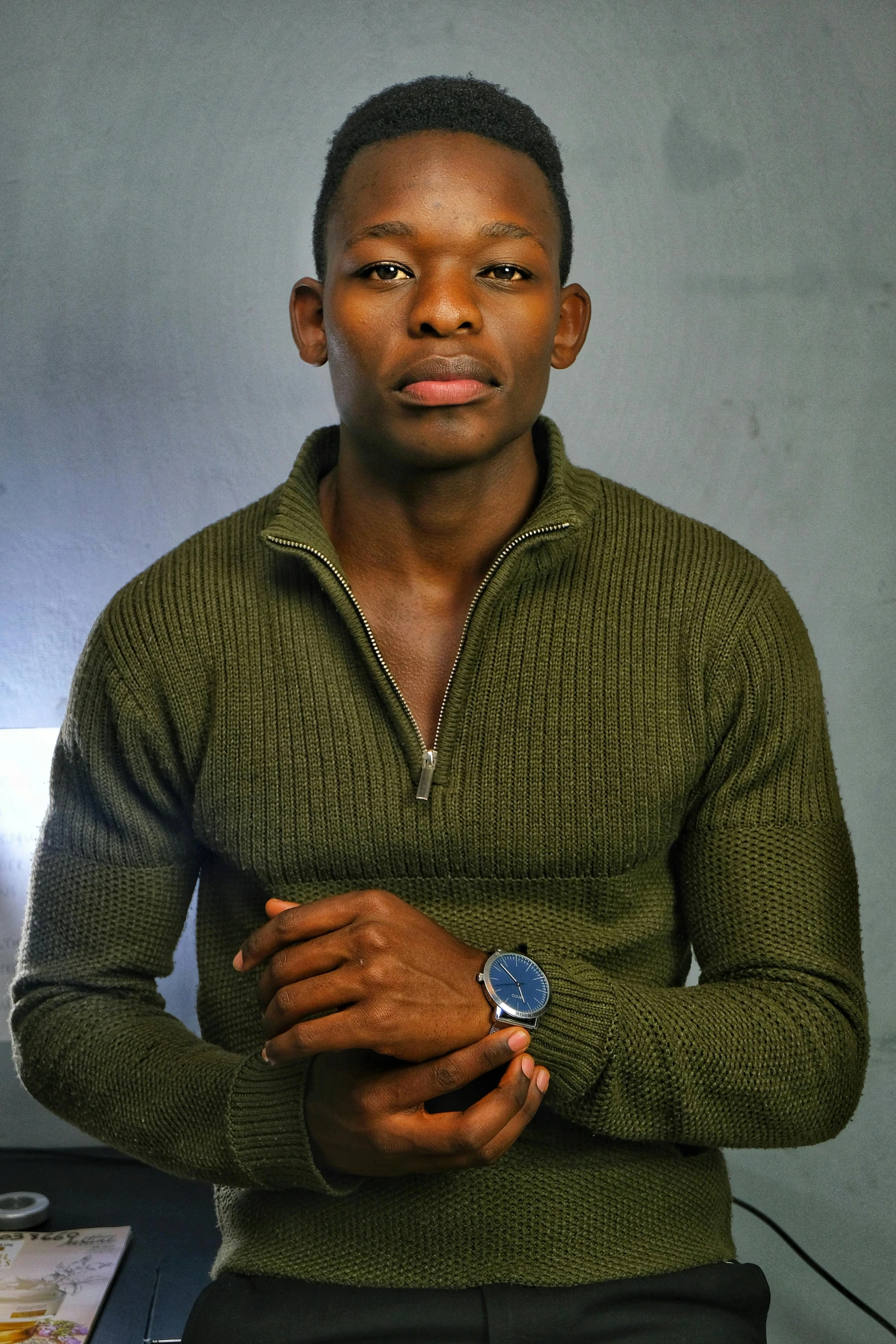 man in green sweater looking sideways and holding watch