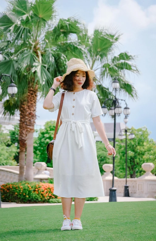 woman in white dress and straw hat standing near palm trees