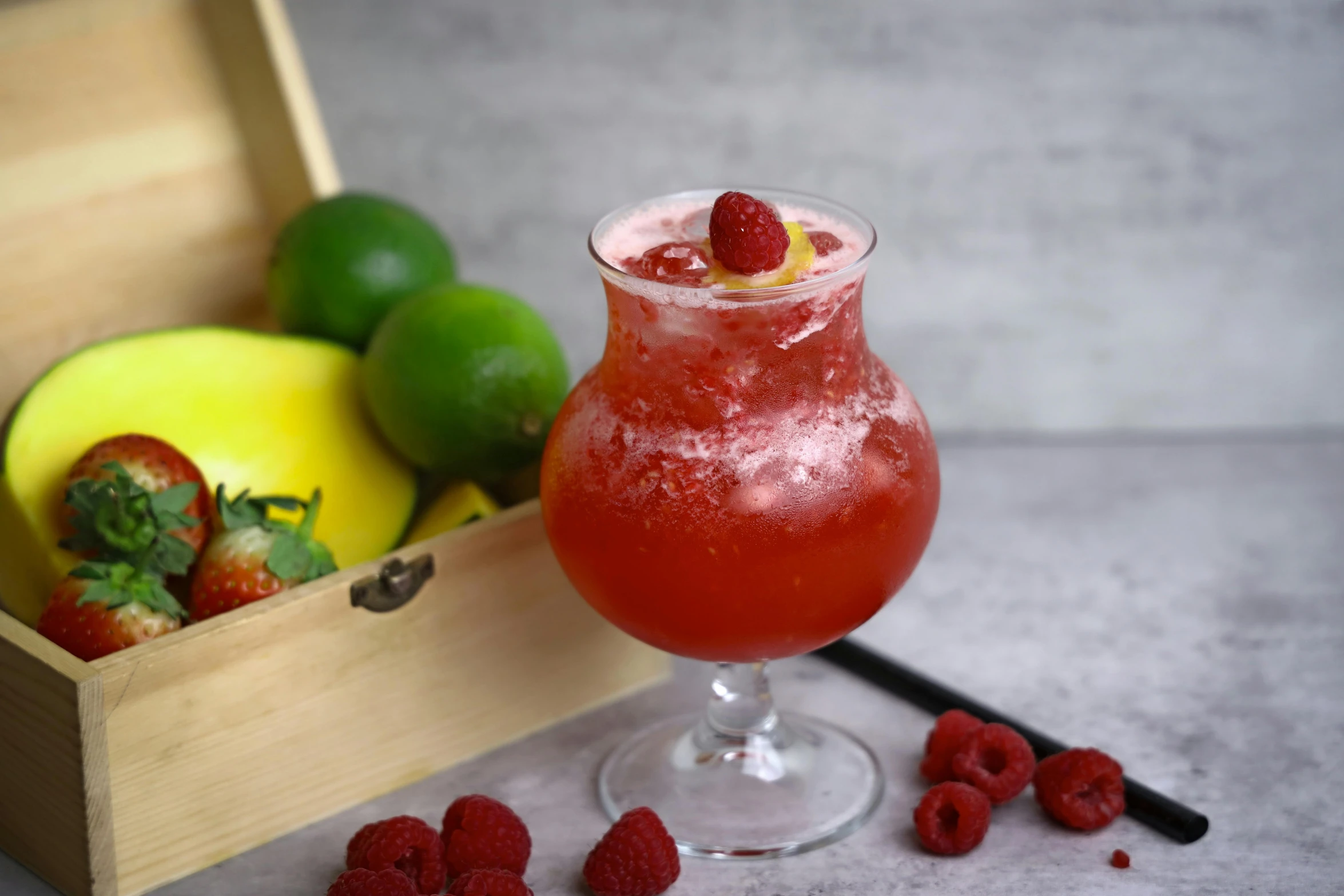 the drink in the glass is garnished with fresh raspberries