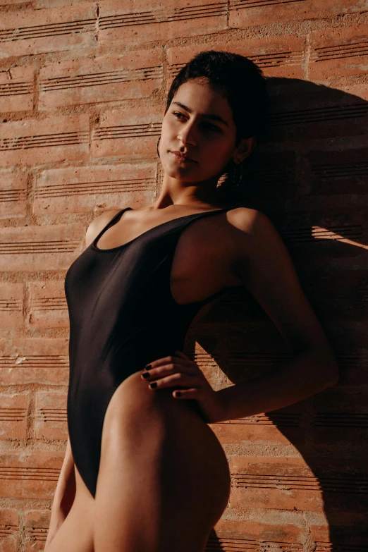 the topless woman in a black swimsuit leaning against a brick wall