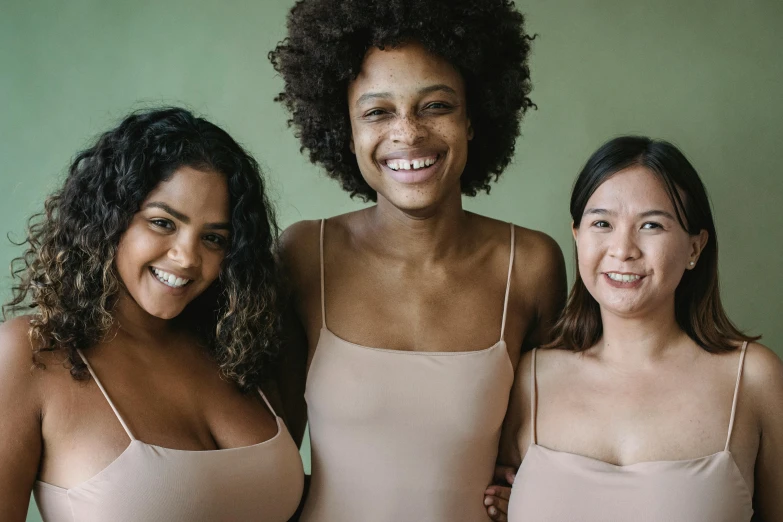 three women smiling while wearing body suits and one has her hands around the other