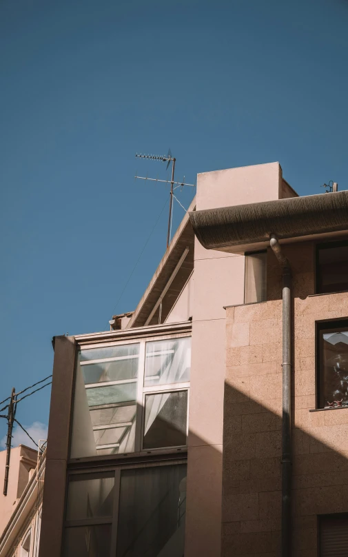 this is an upward view of a very large brown building with a window and an antenna on the roof