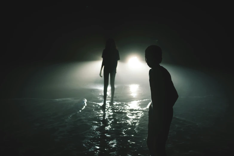 two silhouettes of people standing in the ocean at night