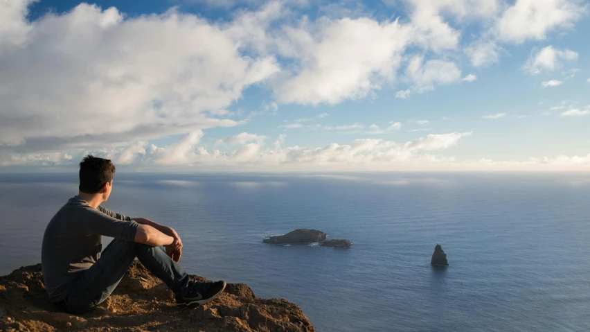 a man sitting on the edge of a cliff near an island