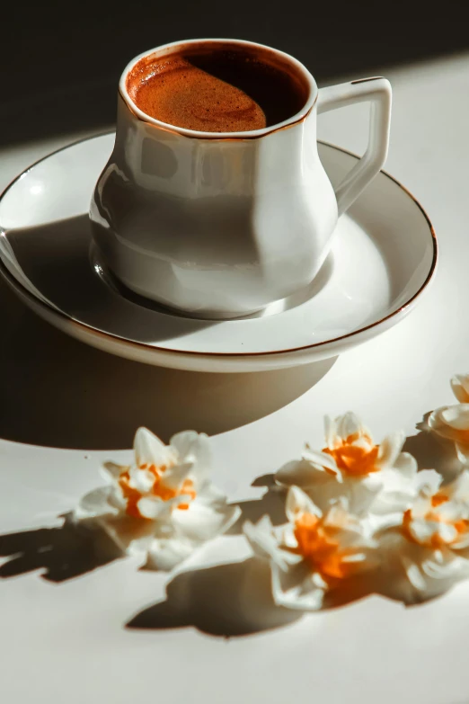 a coffee cup filled with a beverage with white flowers on the table