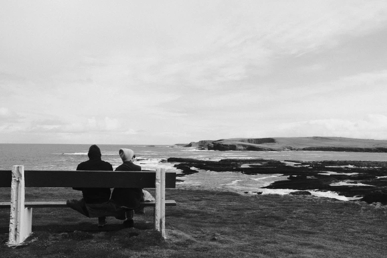 the two people are sitting on a bench at the beach