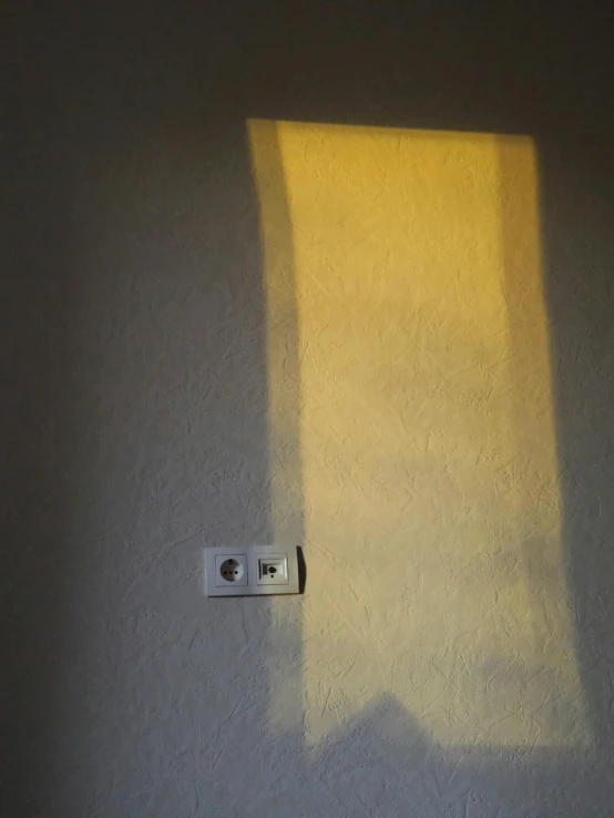 a wall with an electrical outlet and yellow light streaming from behind