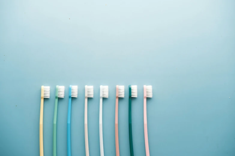 four colorful tooth brushes laid out side by side on a blue background