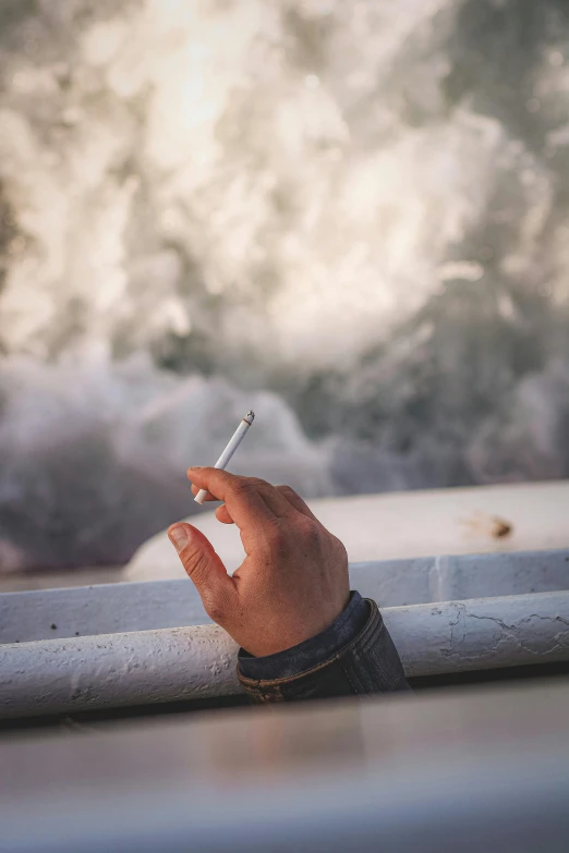 a hand with a cigarette sitting on top of a metal railing