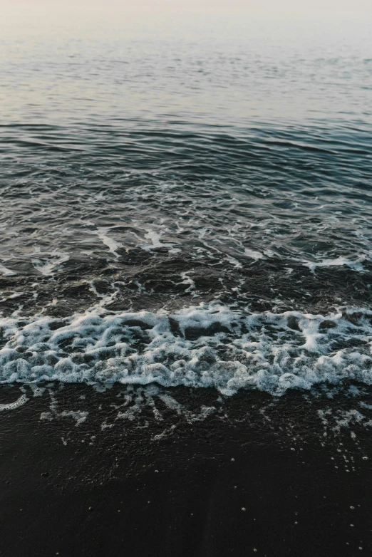 close up of the water and black sand on a beach