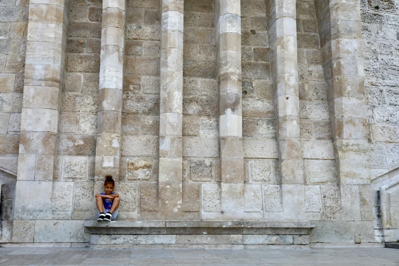 a woman is sitting alone on a curb with her skateboard