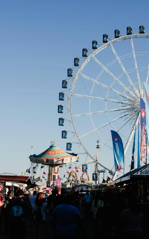 people walking around an carnival with the ferris wheel in view