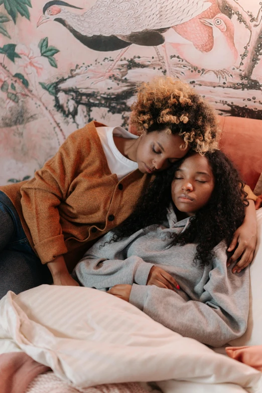 two woman who are laying in bed, one of them has her head on her other side