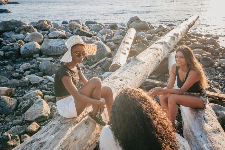 three young women are sitting on logs near the water