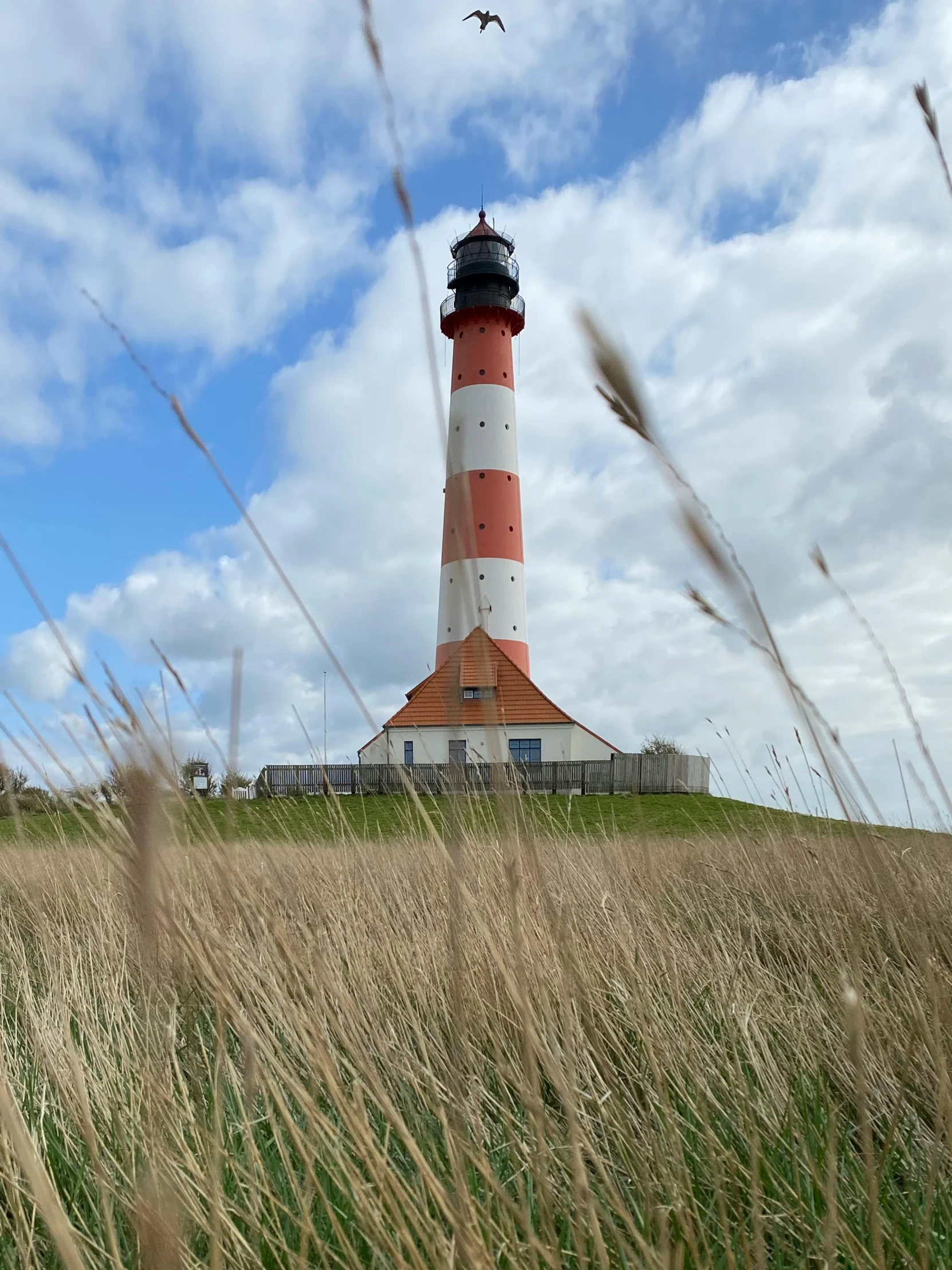 a plane flying in the blue cloudy sky near a light house