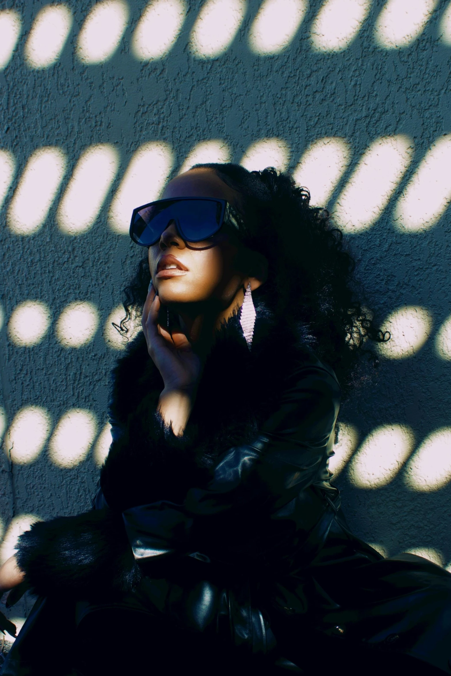 woman wearing shades leaning against wall next to wall with light