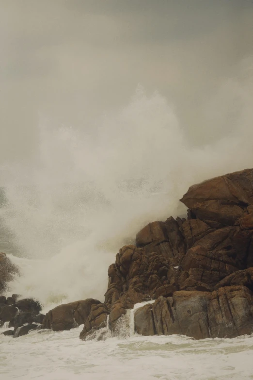 a large wave hits over rocks into shore