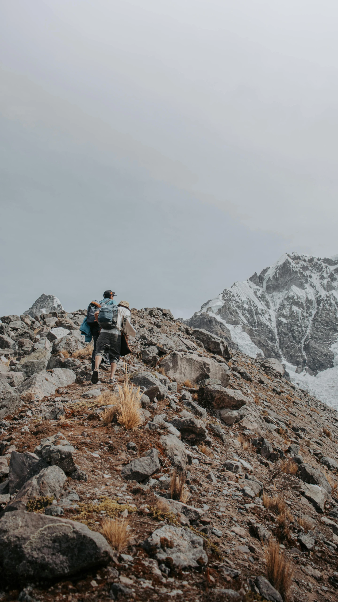 two men hike up a rocky hill side in a cloudy sky