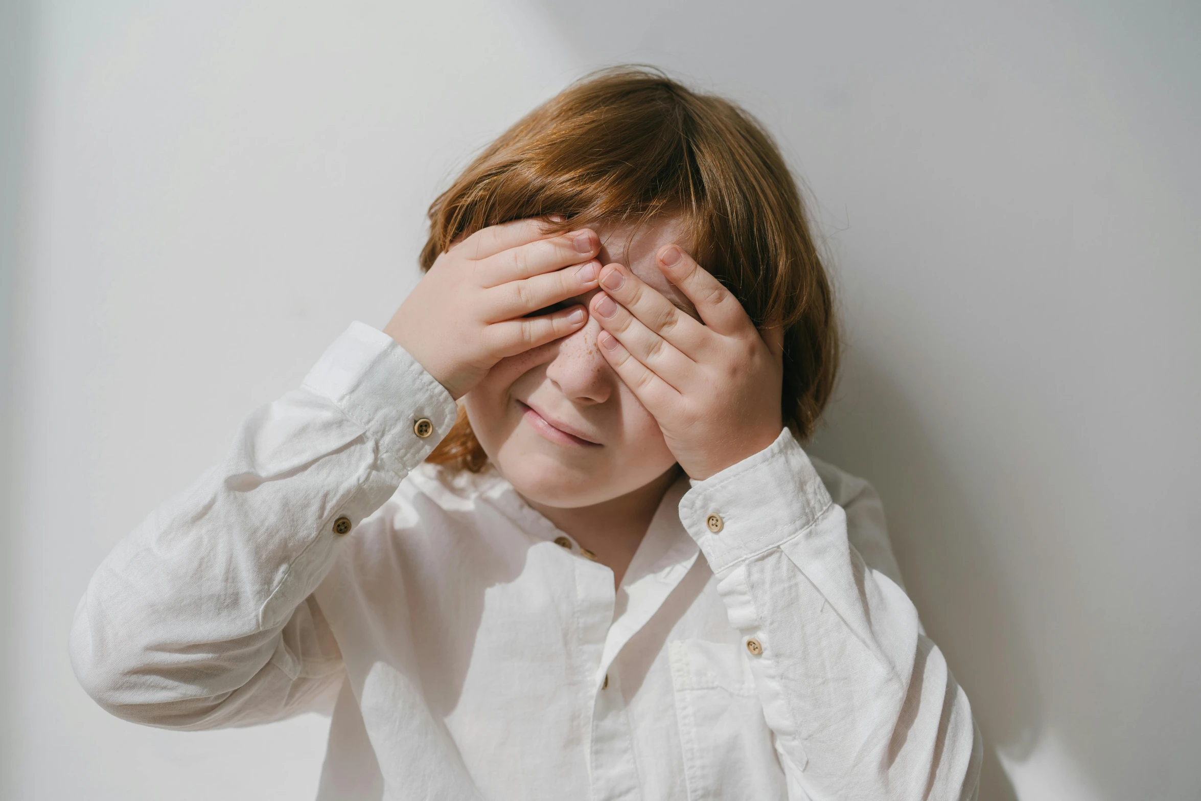 a girl covers her eyes by the side of a wall