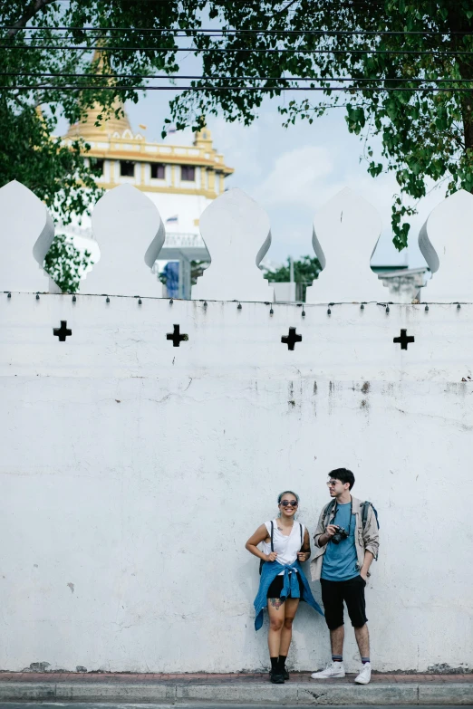 two people leaning against a wall with an elaborate gate in the background