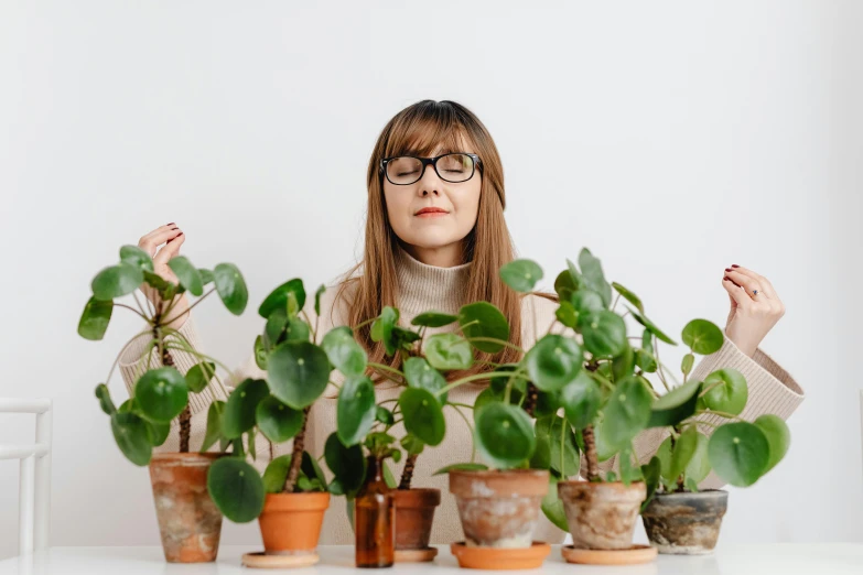 a girl in glasses is standing between several potted plants