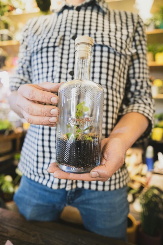 the man is holding a glass bottle filled with plants