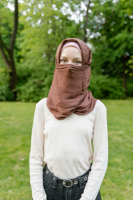 a woman standing in the grass with a brown cowgirl's face covered