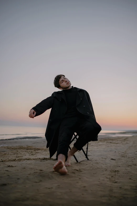 a man wearing a jacket and pants sitting on top of a chair on a beach