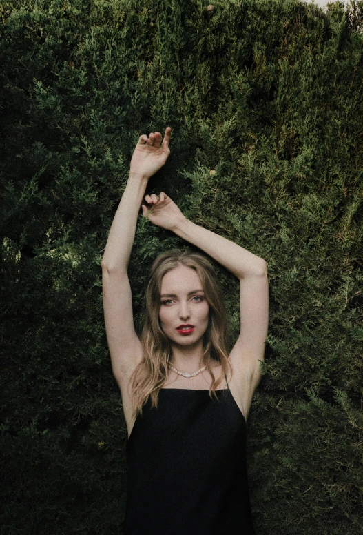 a woman standing with arms raised in front of shrubbery