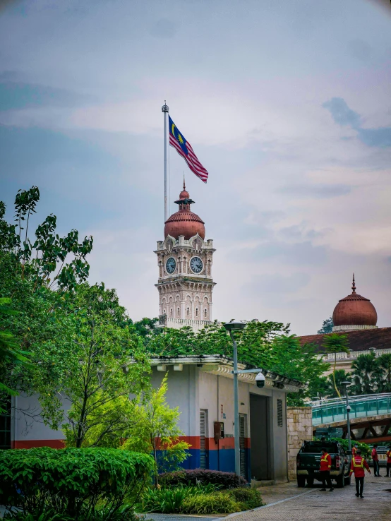 the clock tower is beside a building that has a flag flying above it