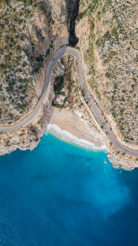 an aerial view of a winding road, next to some clear blue water