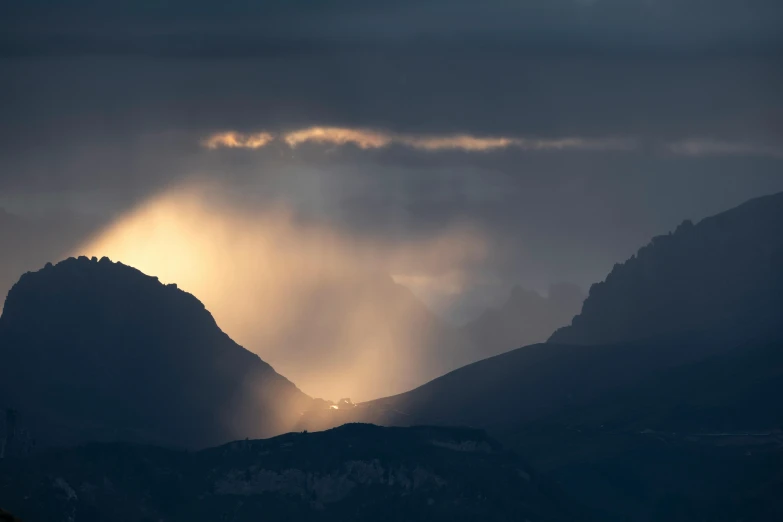 the sun shining through the clouds behind the mountains