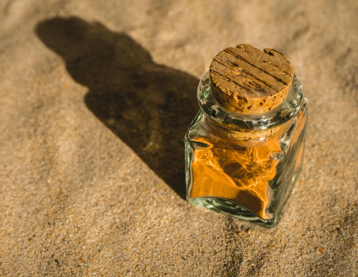 an open bottle filled with sand next to a shadow