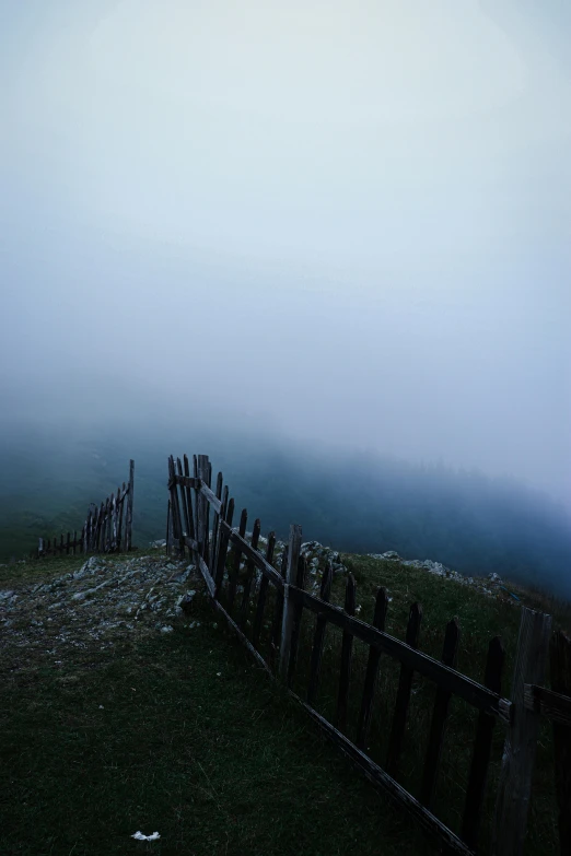 a fence on a grassy area in front of a fog covered sky