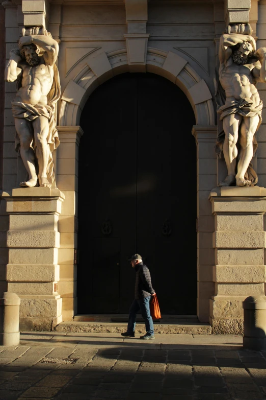 man carrying an orange umbrella walking past arty sculptures