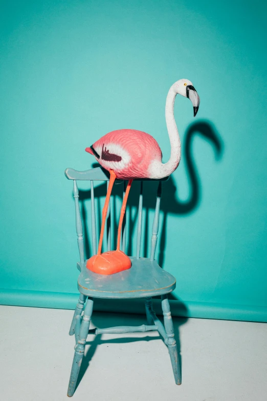 a pink flamingo standing up in a chair with its feet on a yellow ball