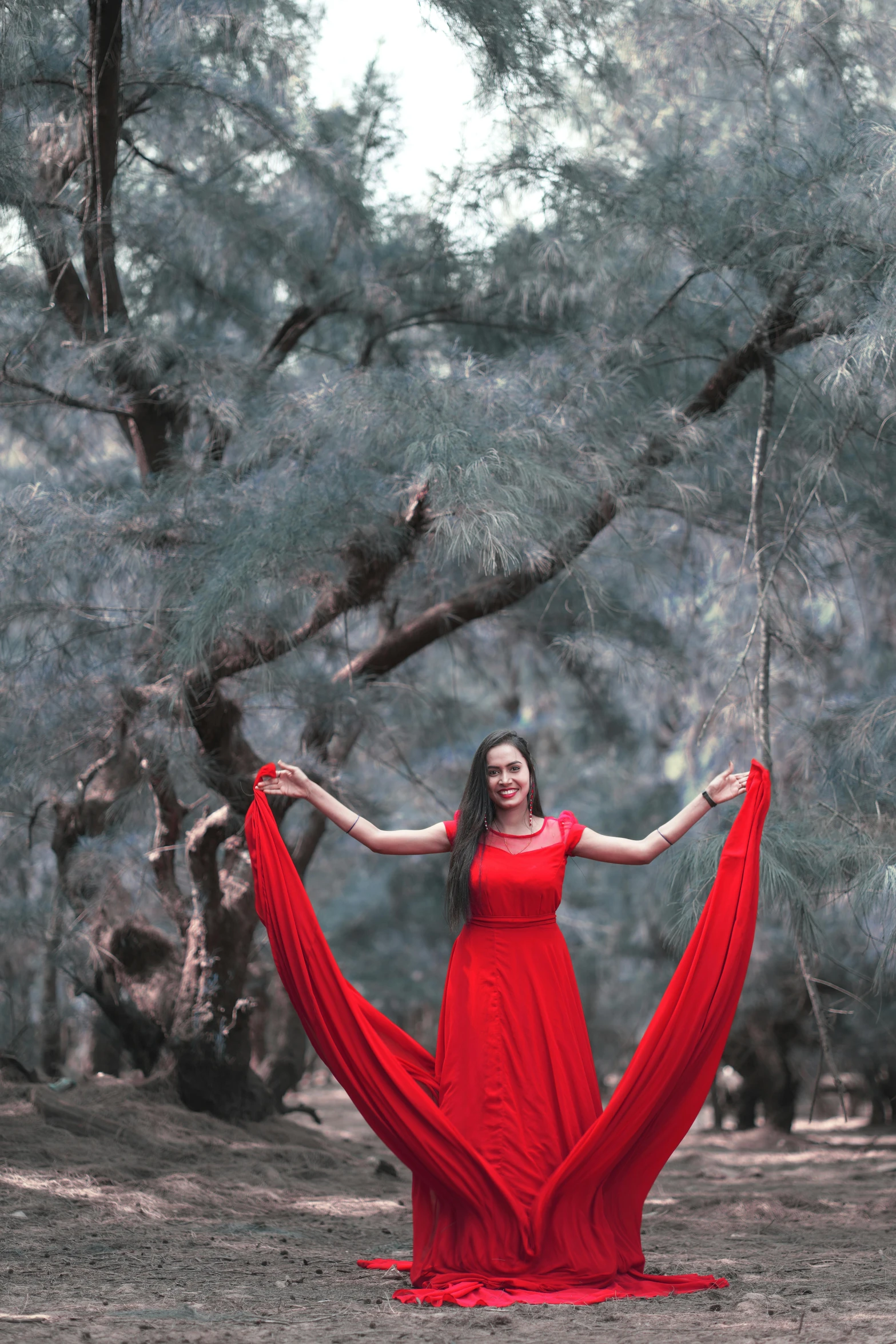 a woman in a red dress poses for a picture in a park