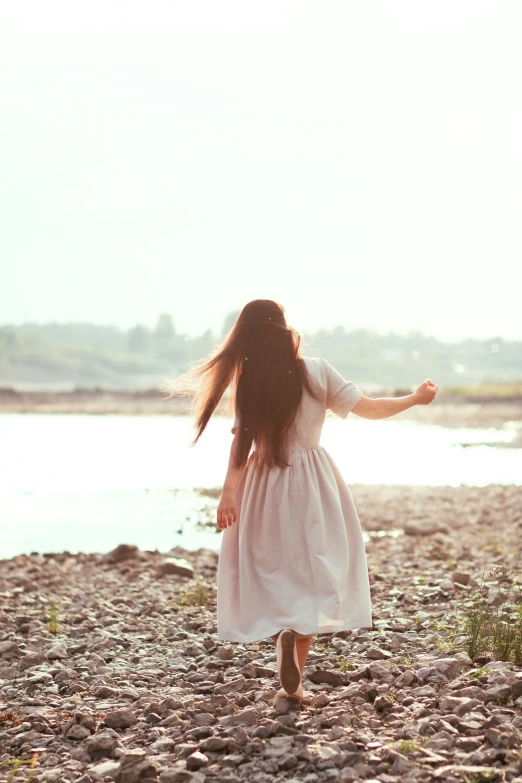 a  in a dress stands on rocks looking at water