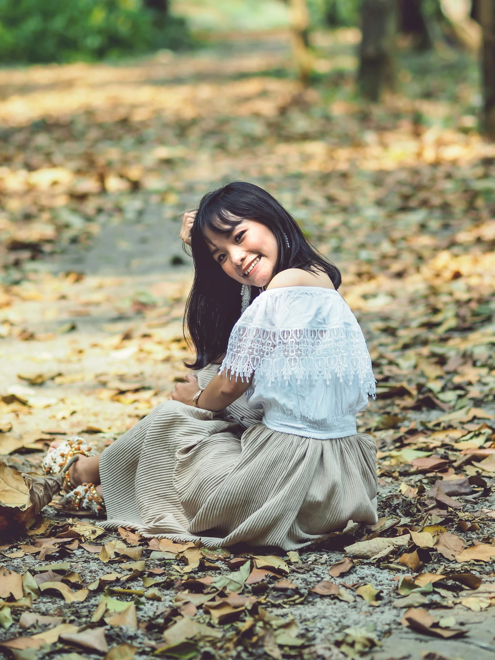 a young woman sits on a path covered in leaves and smiles