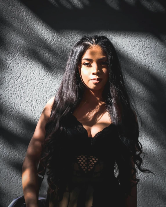 a woman poses against a wall in a black shirt