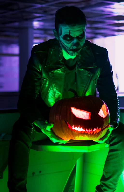 a man in a leather jacket holding a lit jack - o - lantern