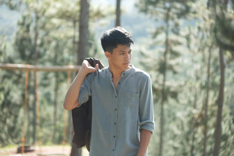 a man stands in front of a forest and holds his coat over his head