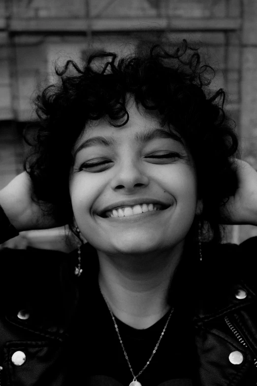 a smiling black - and - white image of a person with curly hair, wearing a necklace