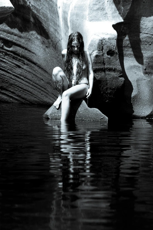 a woman sitting in the water on a rock