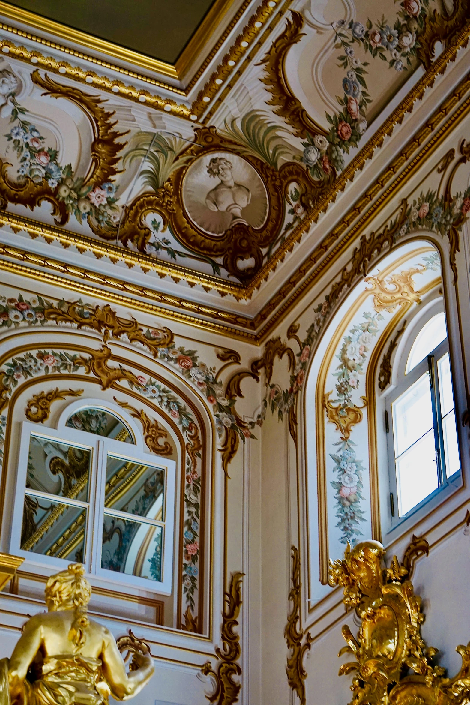a gold clock in front of ornate painted walls